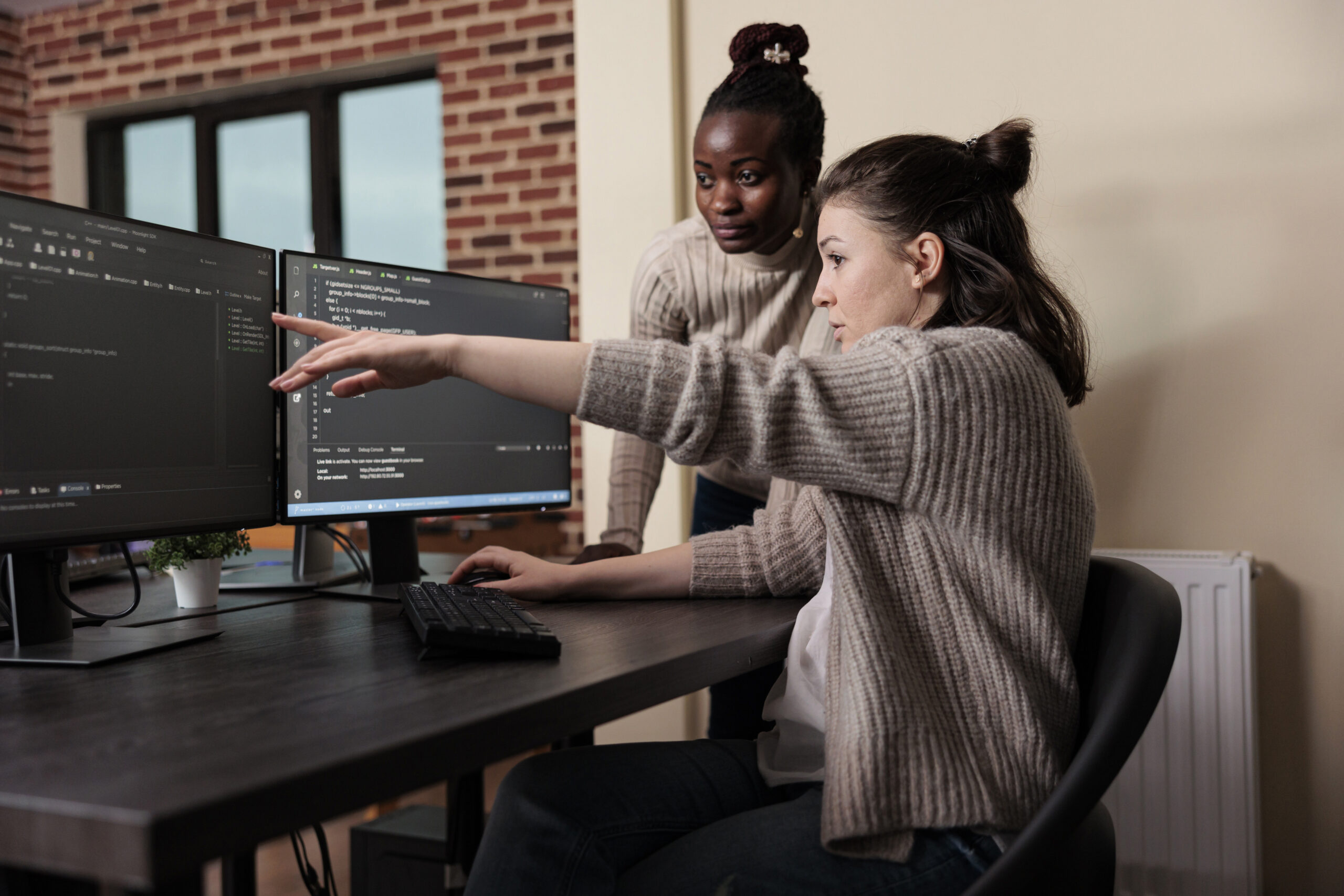 Caucasian network developer pointing out high usage of processing power in mainframe grid. African american programmer helping coworker to solve overloaded system storage space.