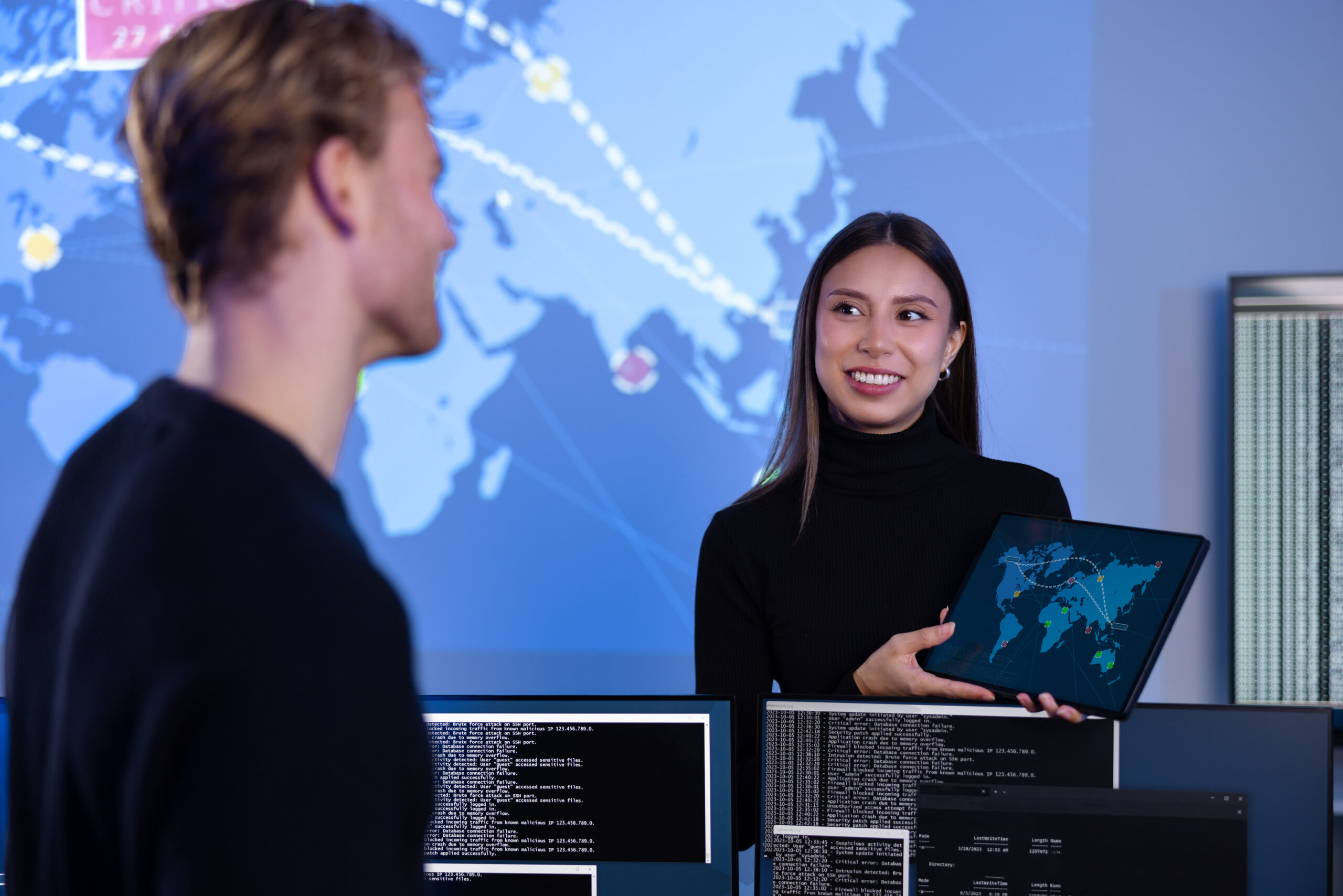 Smiling cyber security team working in a Cyber Security Operations Center (SOC). Woman work as Chief Information Security Officer (CISO) and manager pointing on a real time map om tablet.